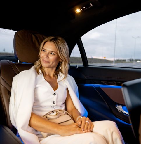 Elegant businesswoman sitting on backseat of luxury car on evening